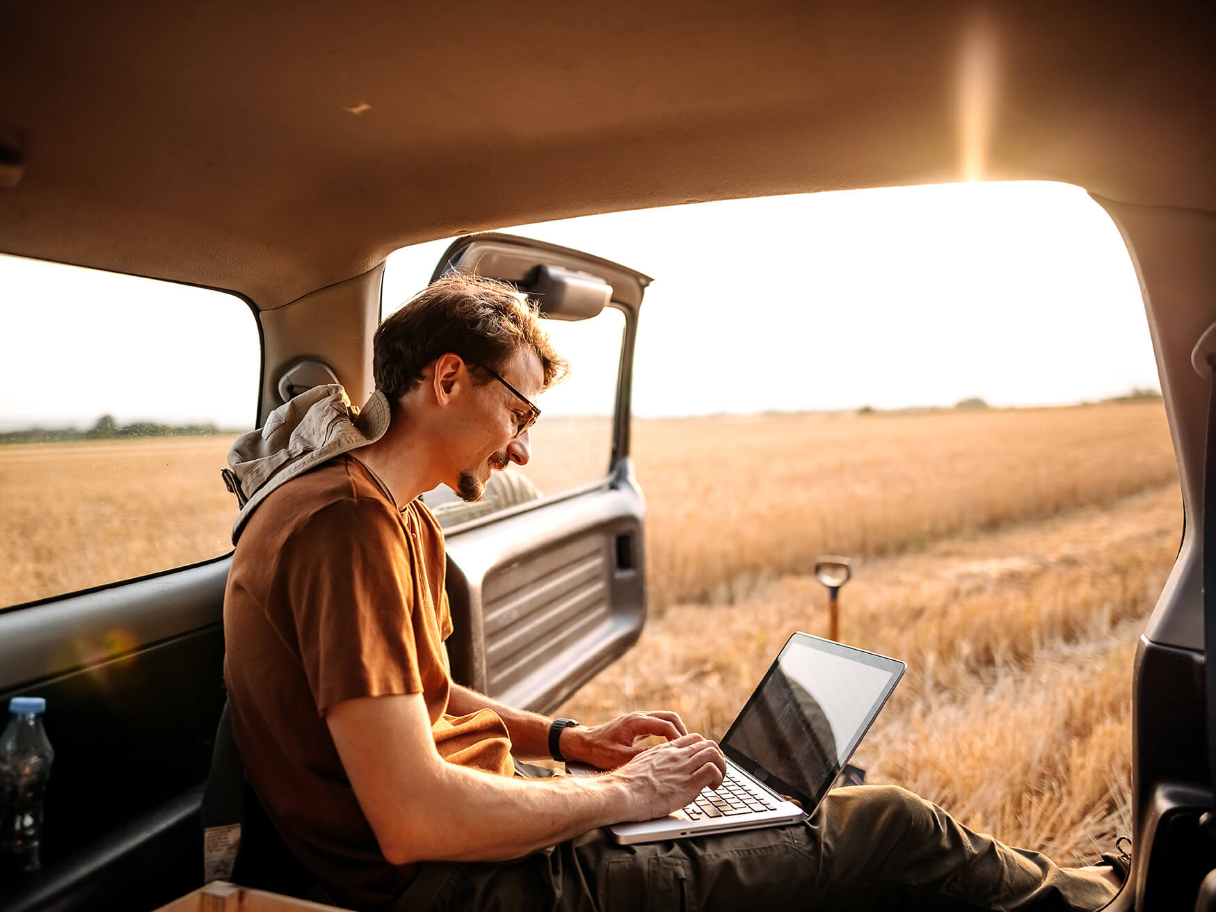 Man in car using laptop in middle of field