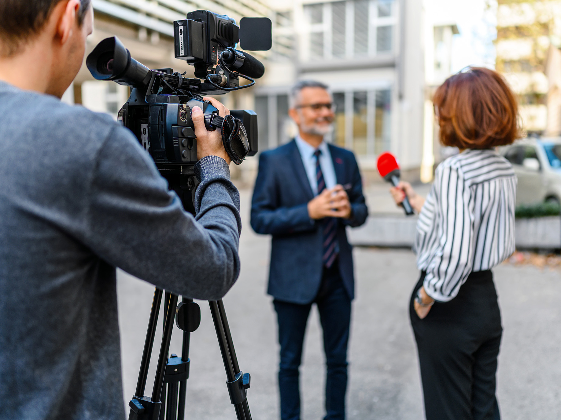 A cameraman and woman with microphone interviewing man in suit