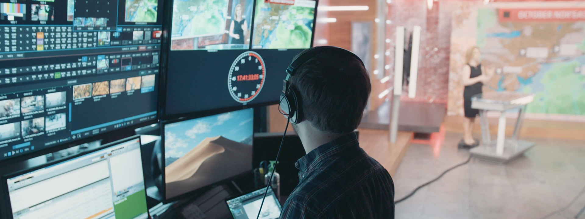 Person wearing headphones monitoring screens of weather broadcast