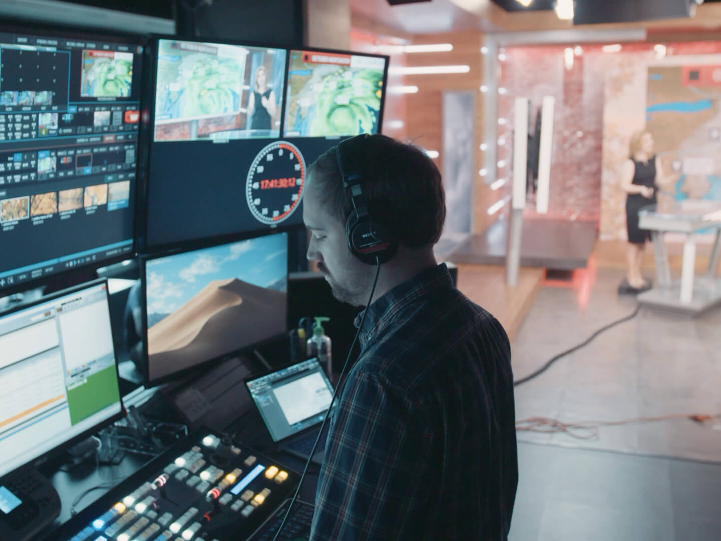 Person wearing headphones monitoring screens of weather broadcast