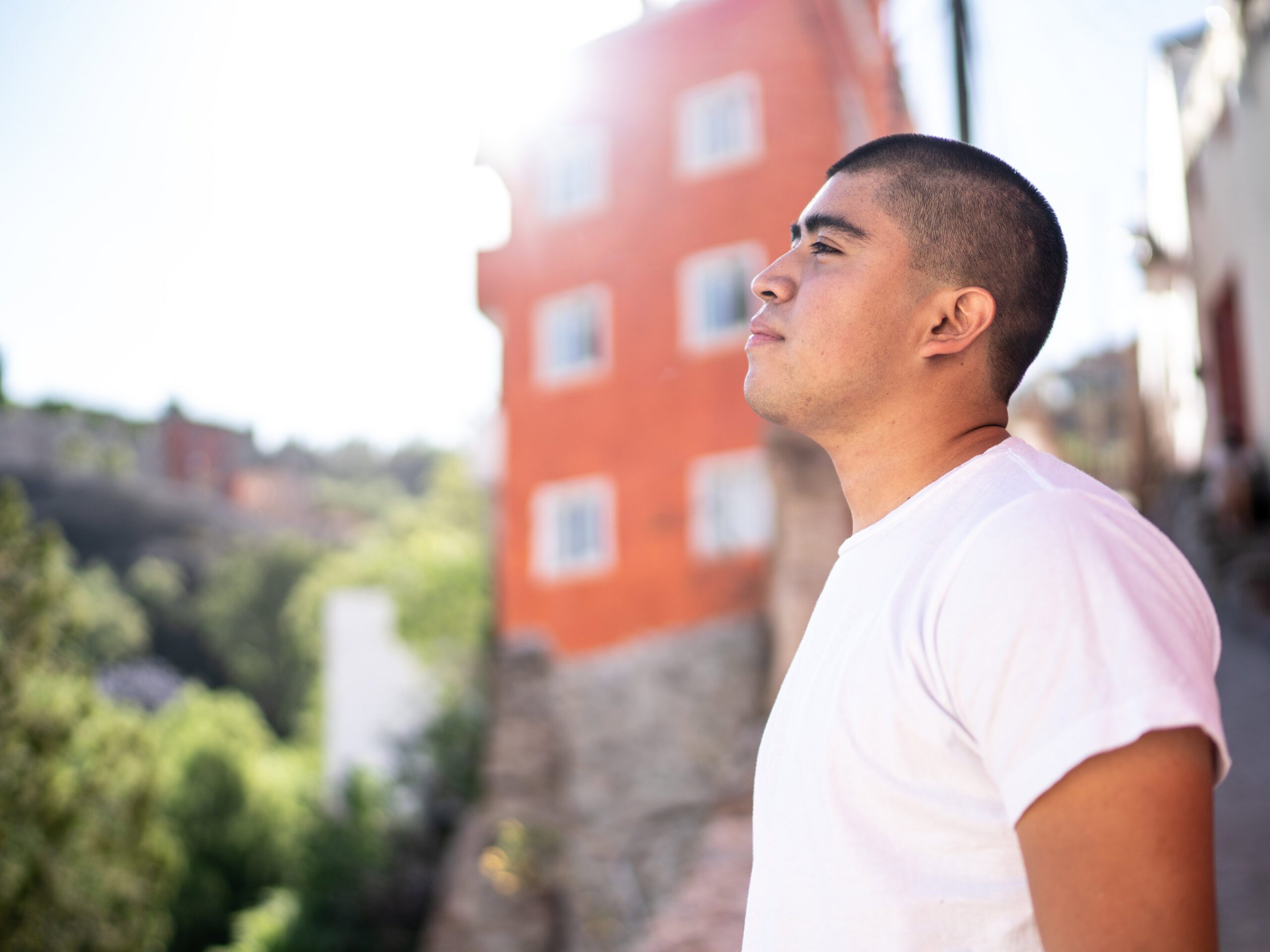 Young hispanic man outdoors with sun shining looking away contemplating