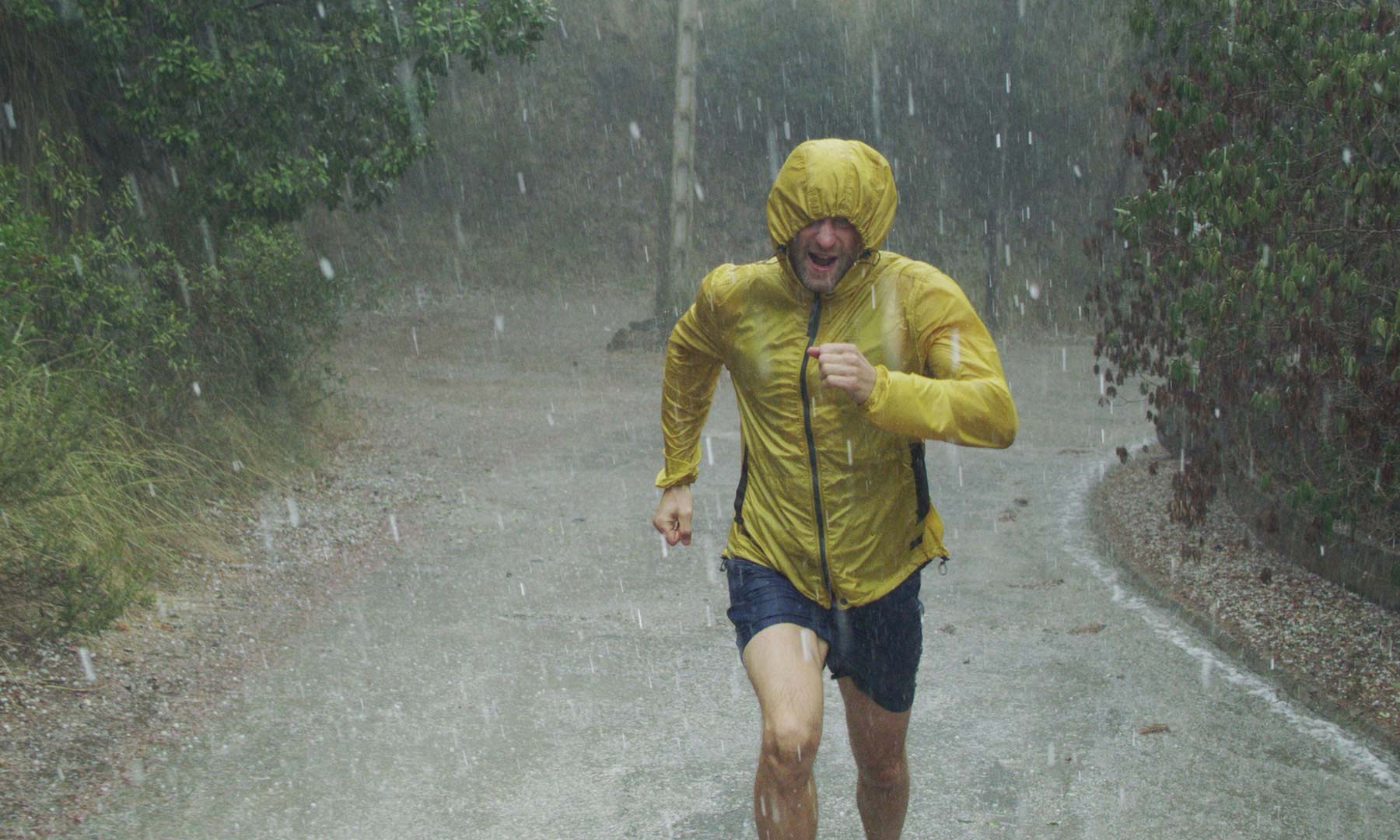 Man running in the rain with a yellow raincoat on.