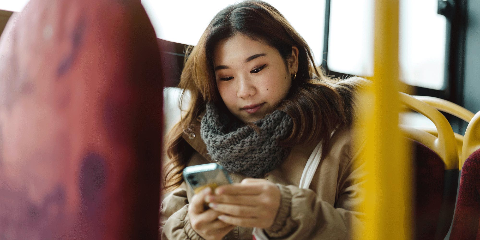 Asian woman riding a bus looking at her phone.