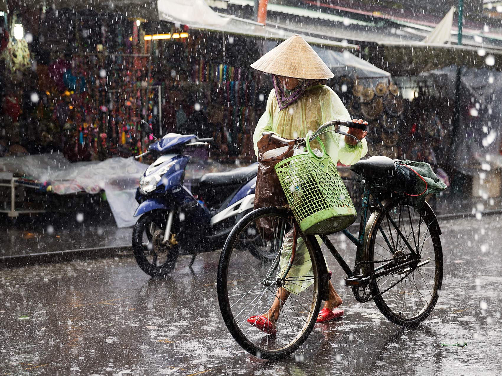 Woman walking bicycle along in pouring rain with pointed hat in Vietnam