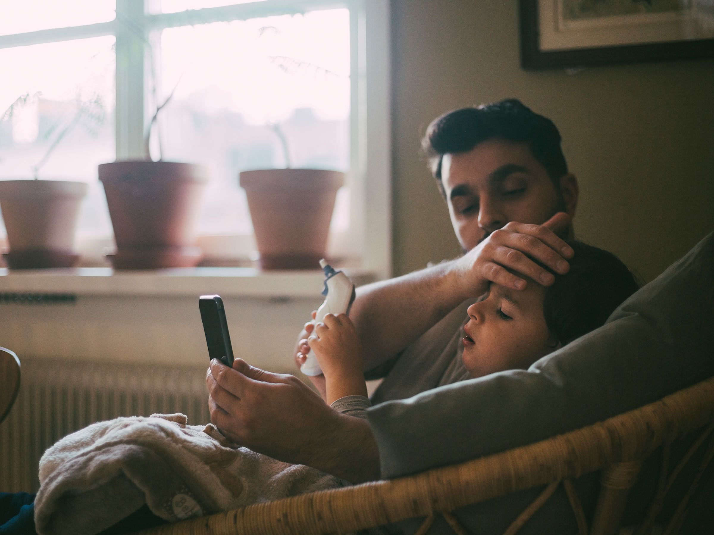 Father checking temperature of son while sitting in living room at home