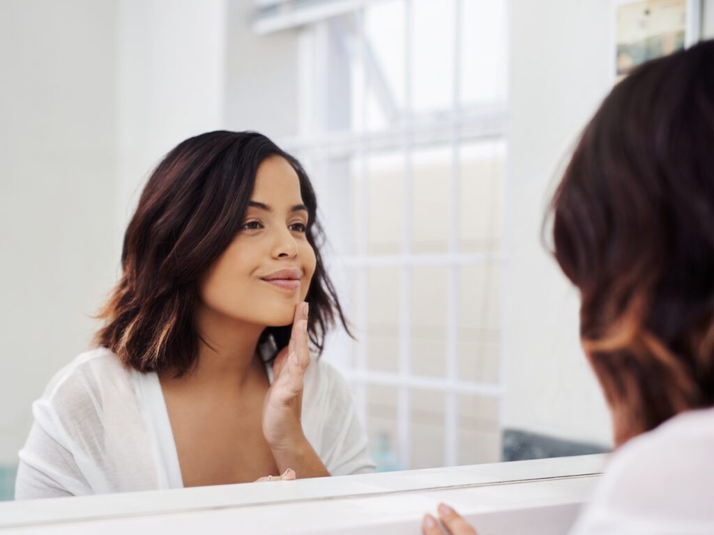 Woman looking at skin in bathroom mirror