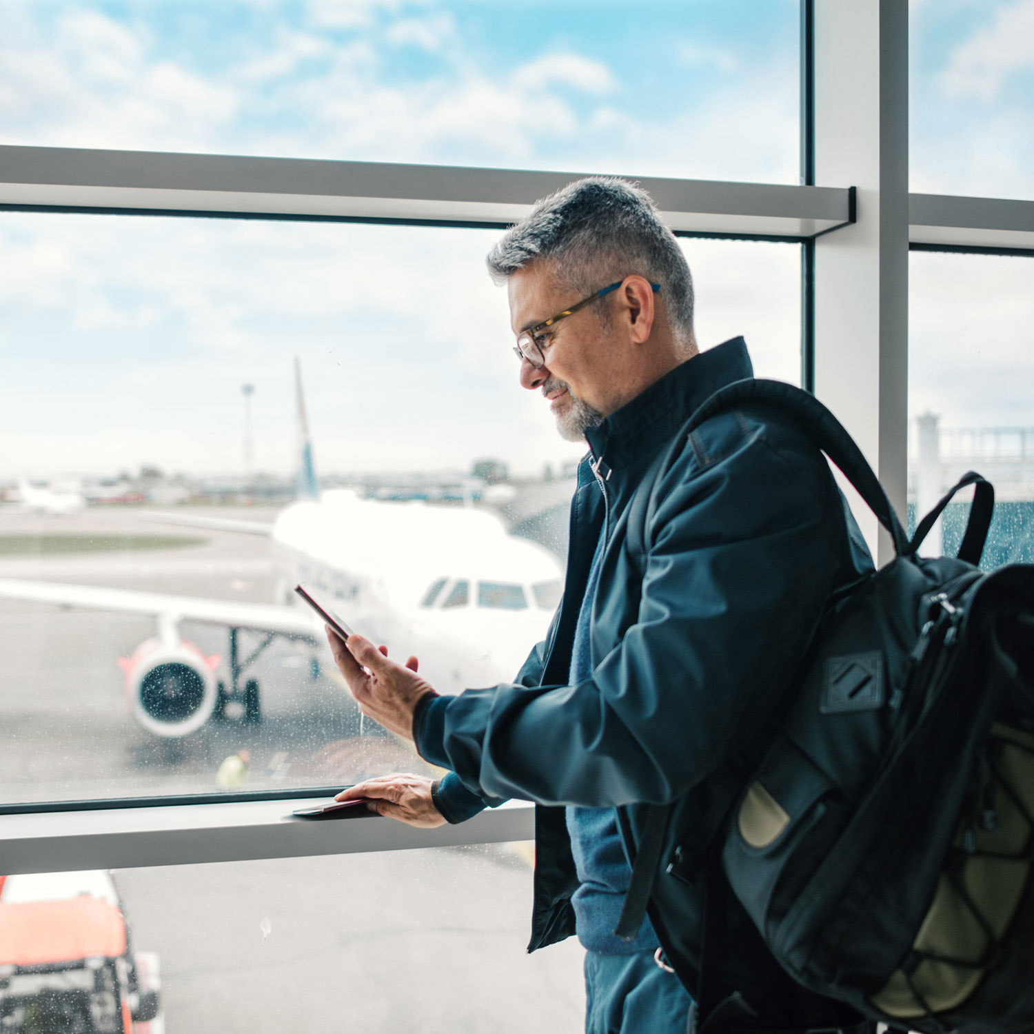 Man waiting for his flight in airport lounge looking at his phone.