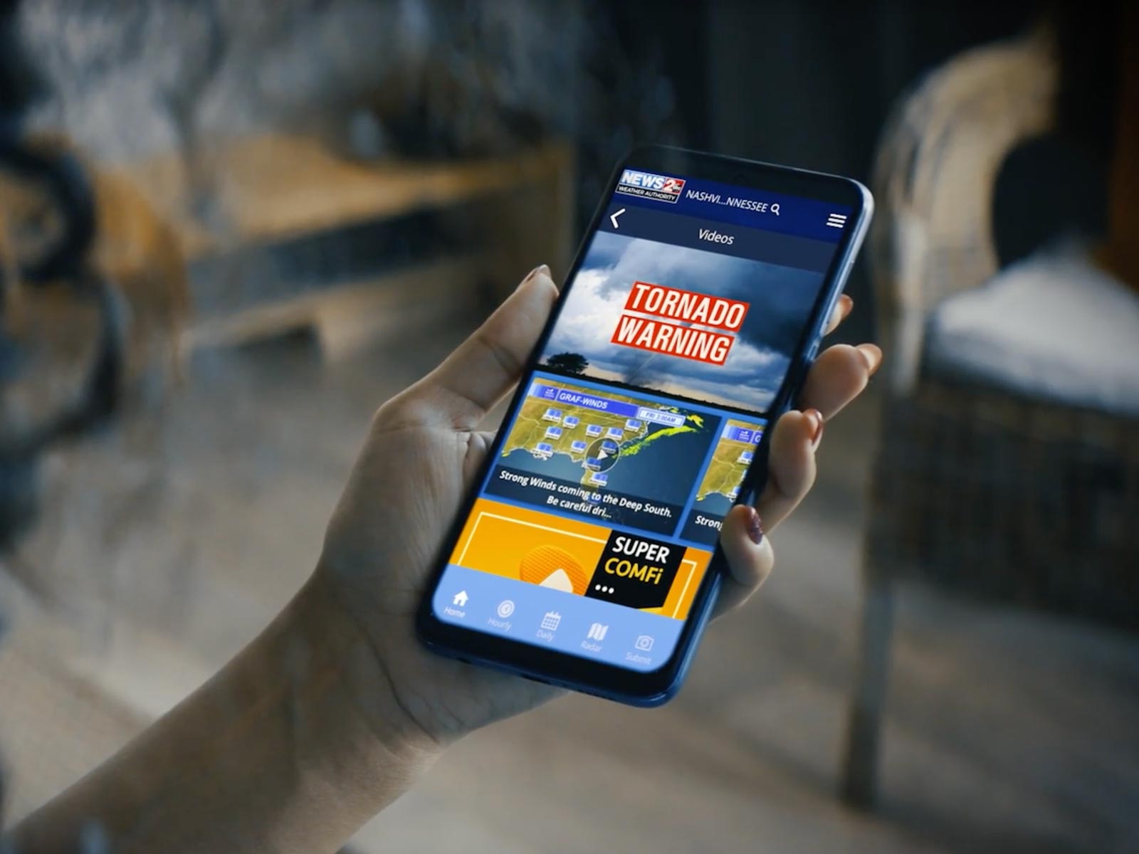 woman looking at phone in her hand that is showing a local weather app with tornado warning.