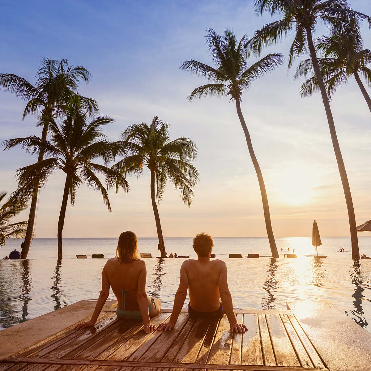 Couple sitting by the pool looking at a sunset with palm trees