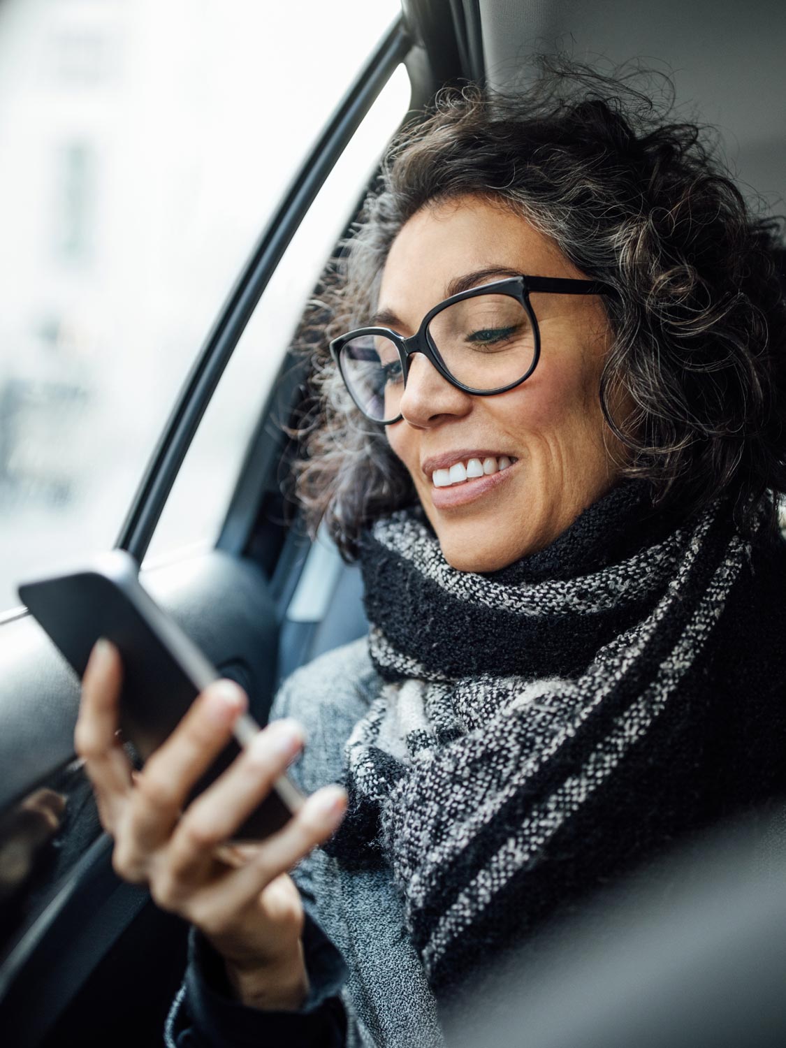 Mature woman looking at her cell phone while traveling in the backseat of a car.