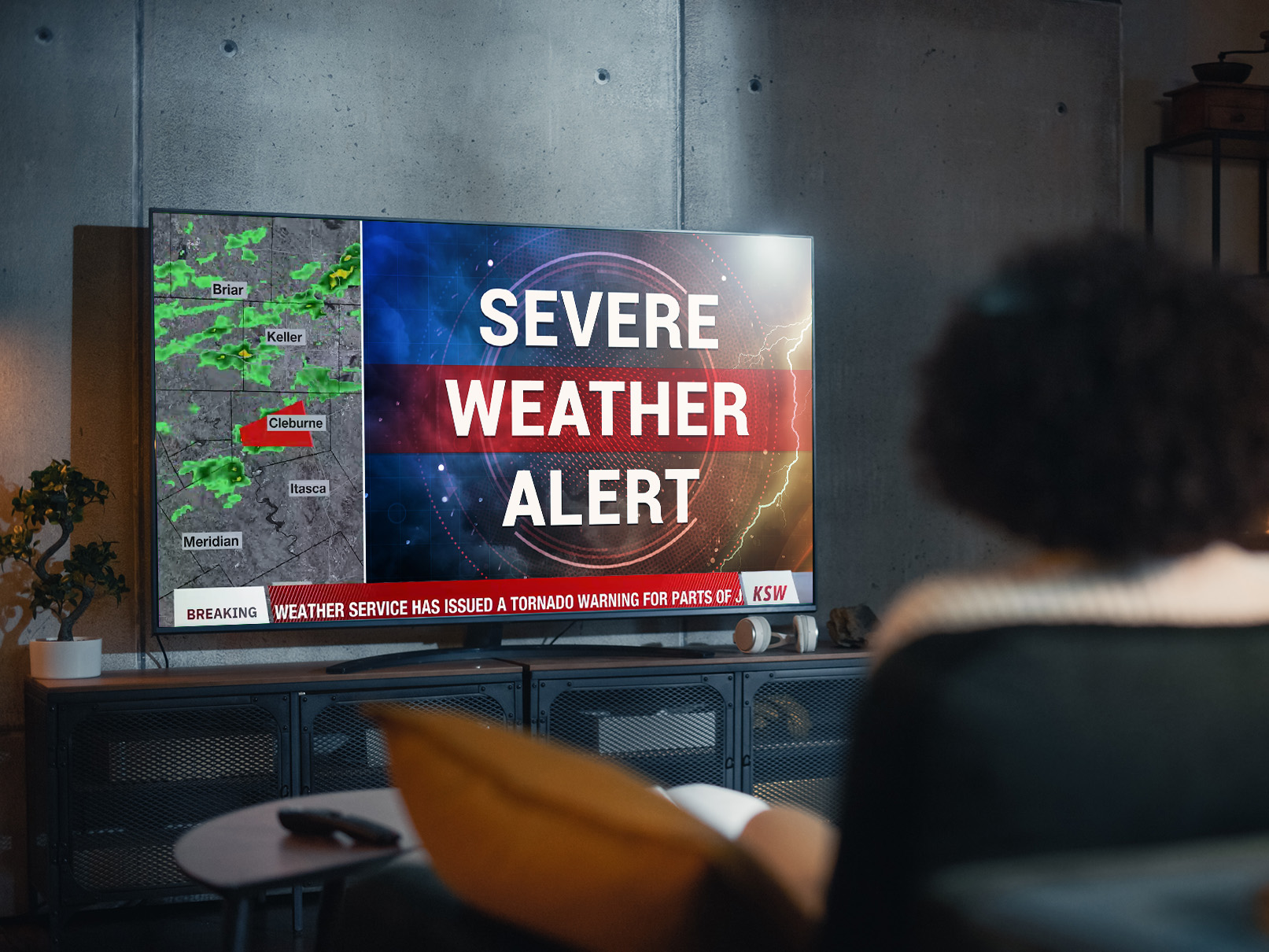Woman on a couch seeing a severe weather alert displayed on her TV.