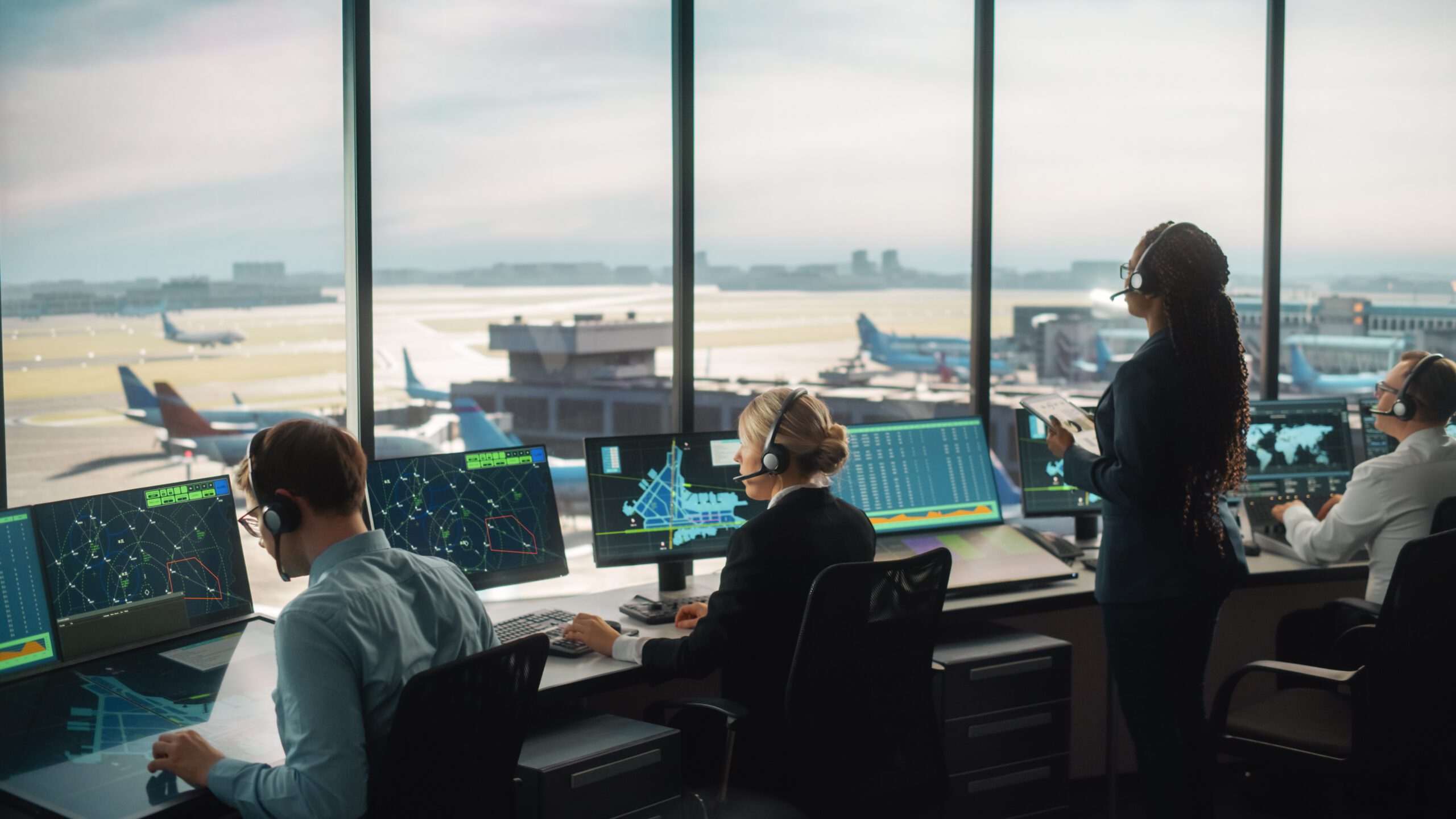 Diverse Air Traffic Control Team Working in a Modern Airport Tower. Office Room is Full of Desktop Computer Displays with Navigation Screens, Airplane Departure and Arrival Data for Controllers.