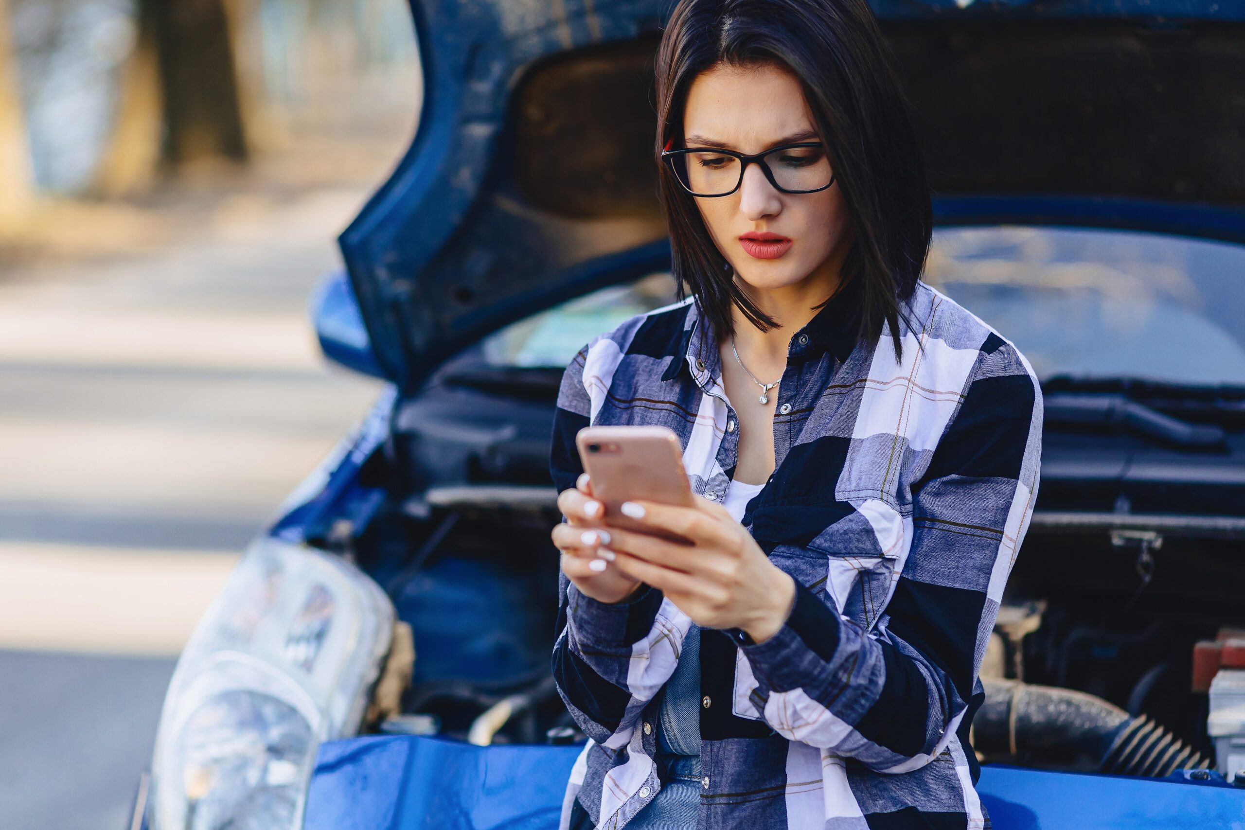 Girl with phone near open hood of car on road