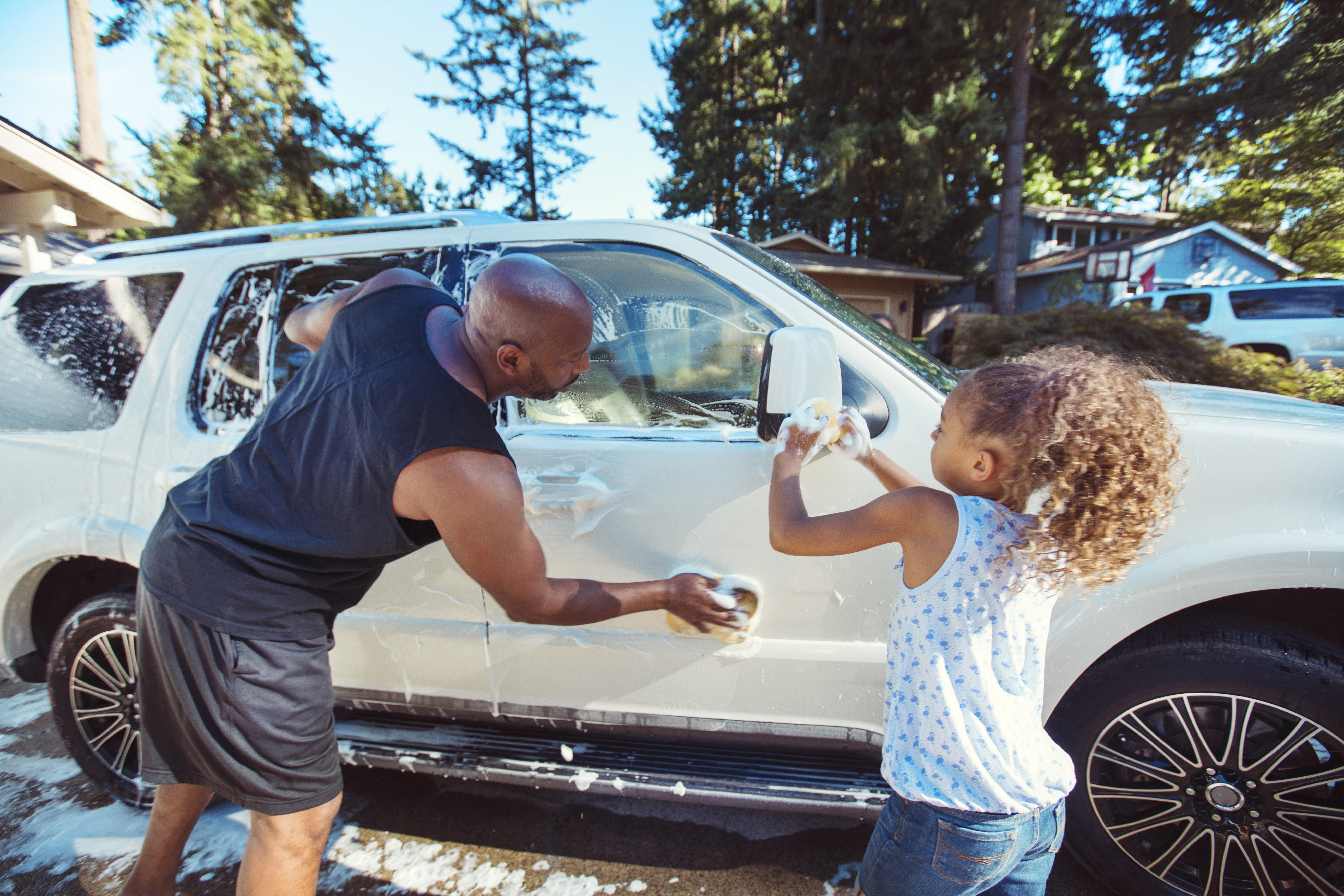 Father and daughter washing car in driveway