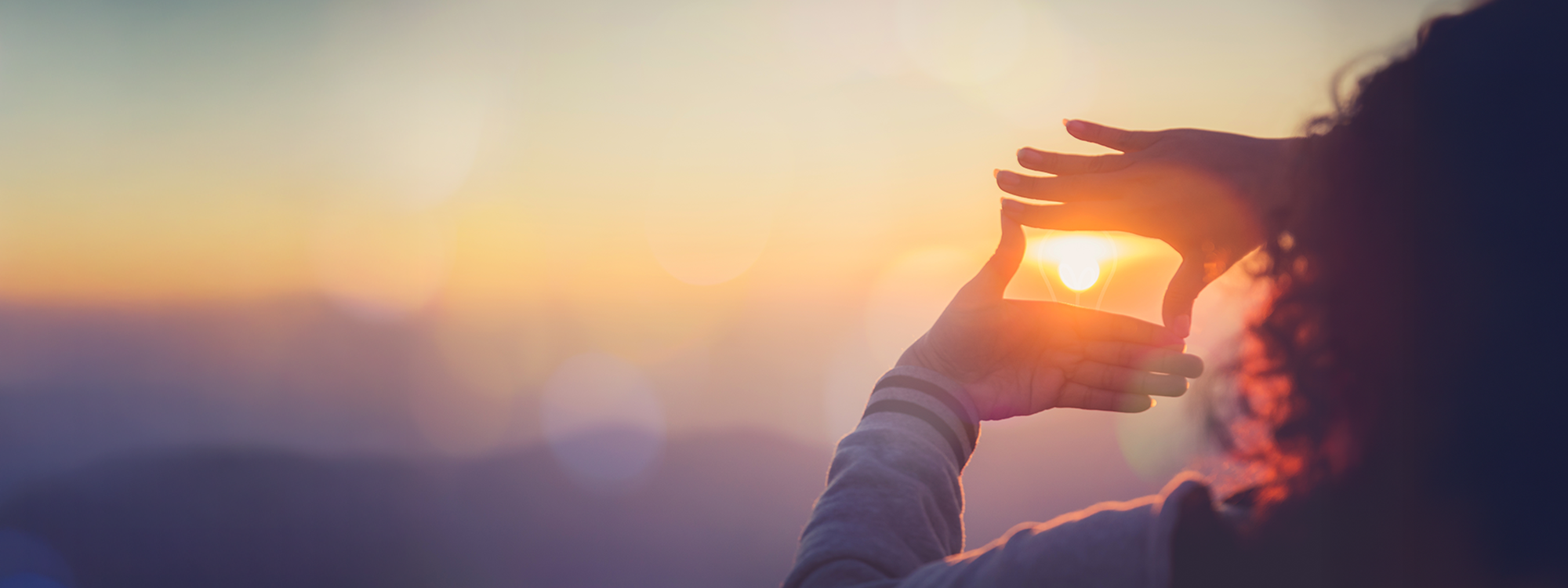 Woman looking up at the sky in the evening cropping the sun with her hands.