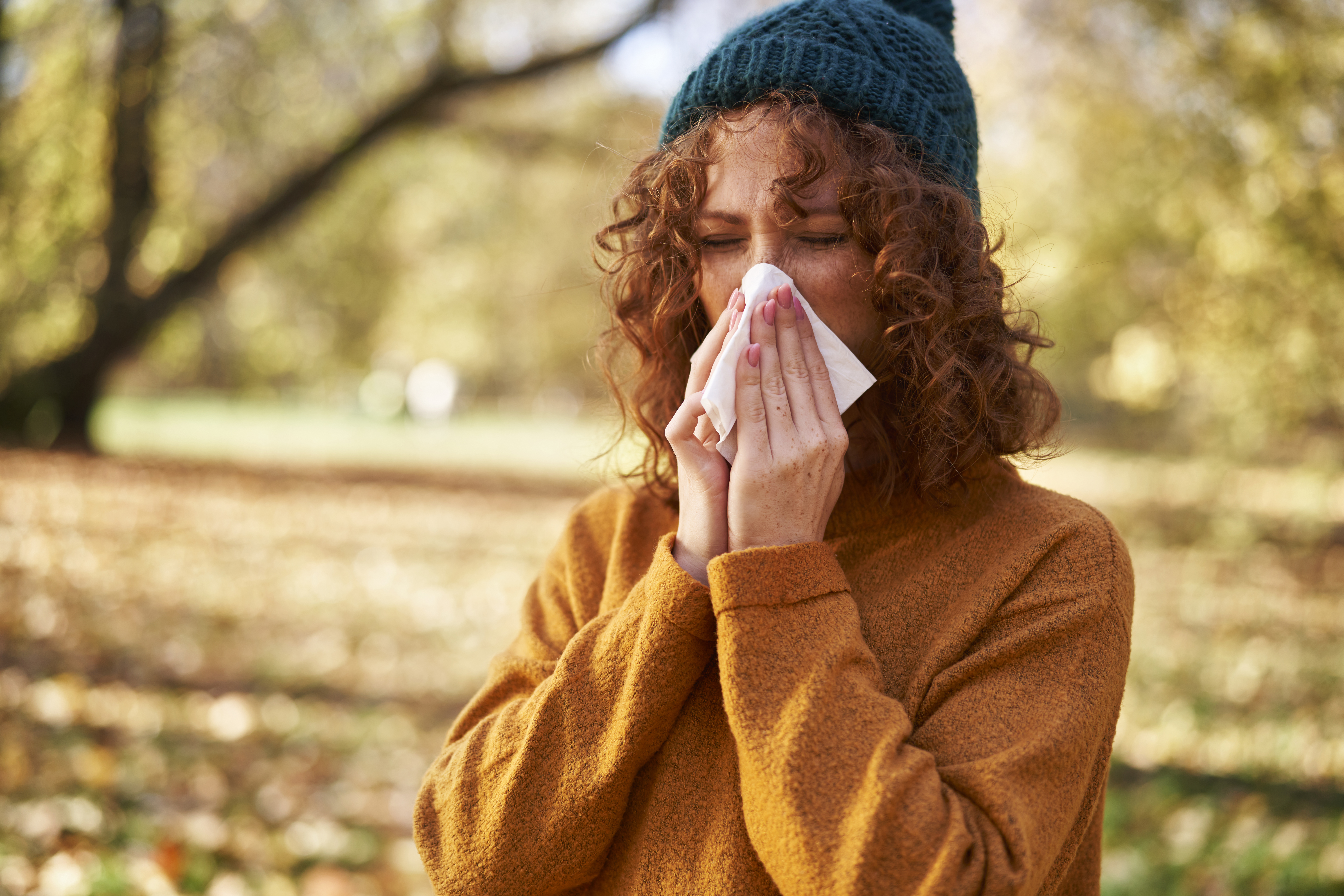 Redhead woman blowing nose with facial tissue at autumn park