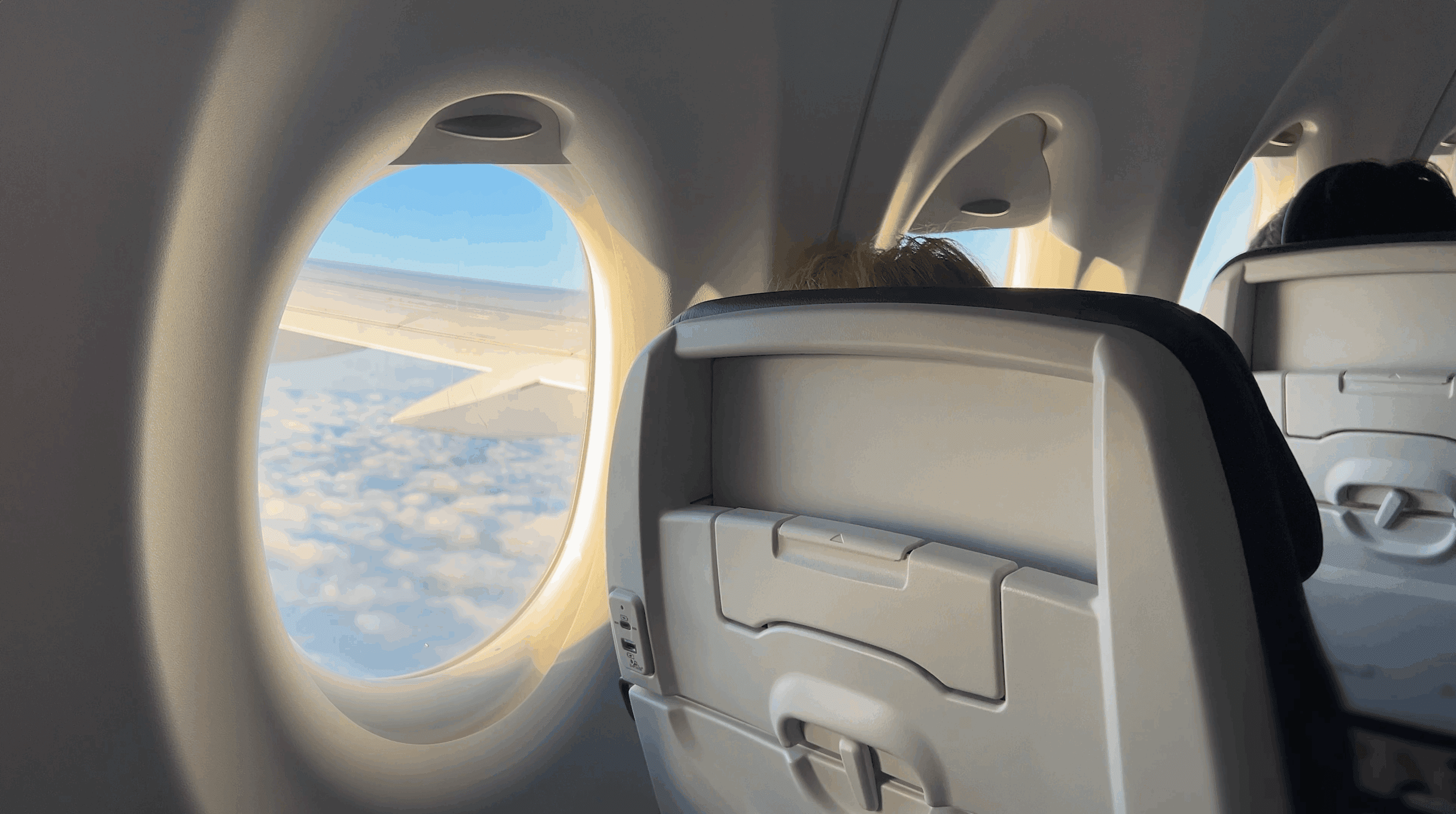 View from the inside of an airplane out through a passenger window to a clear day.