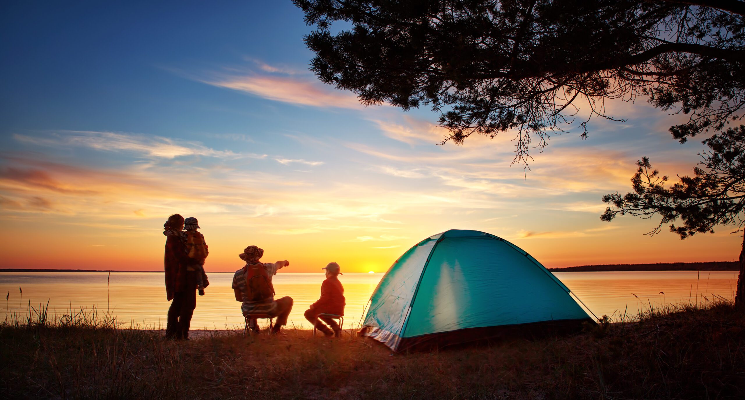 A family outside of their camping tent enjoying a lakeside sunset