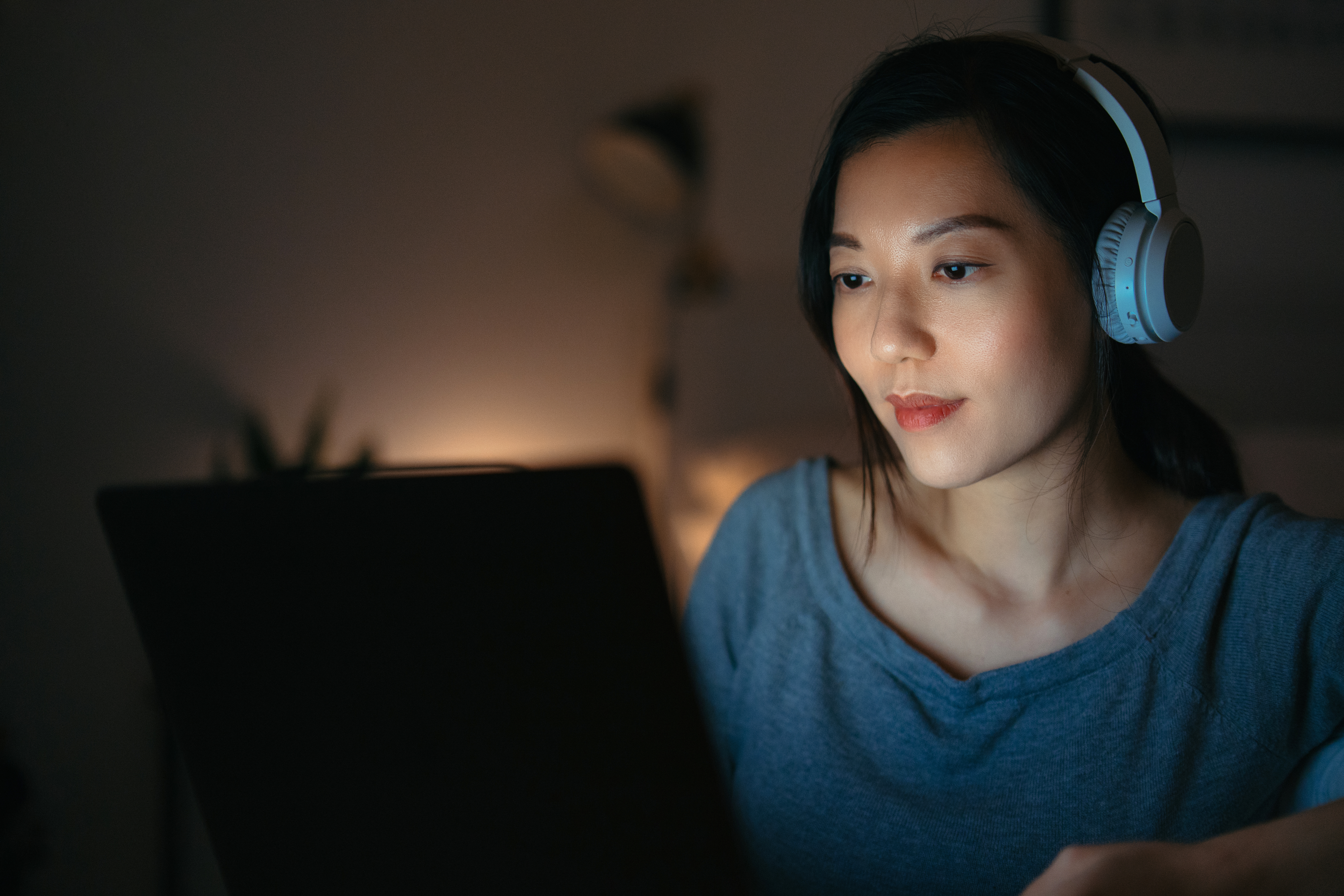 Concentrated young woman wearing headphones watching streaming TV programming on a laptop