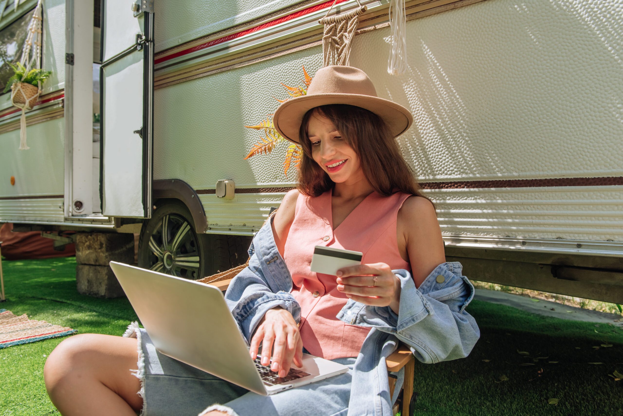 Smiling young woman making credit card repayment via internet outside using laptop while traveling during hot months.