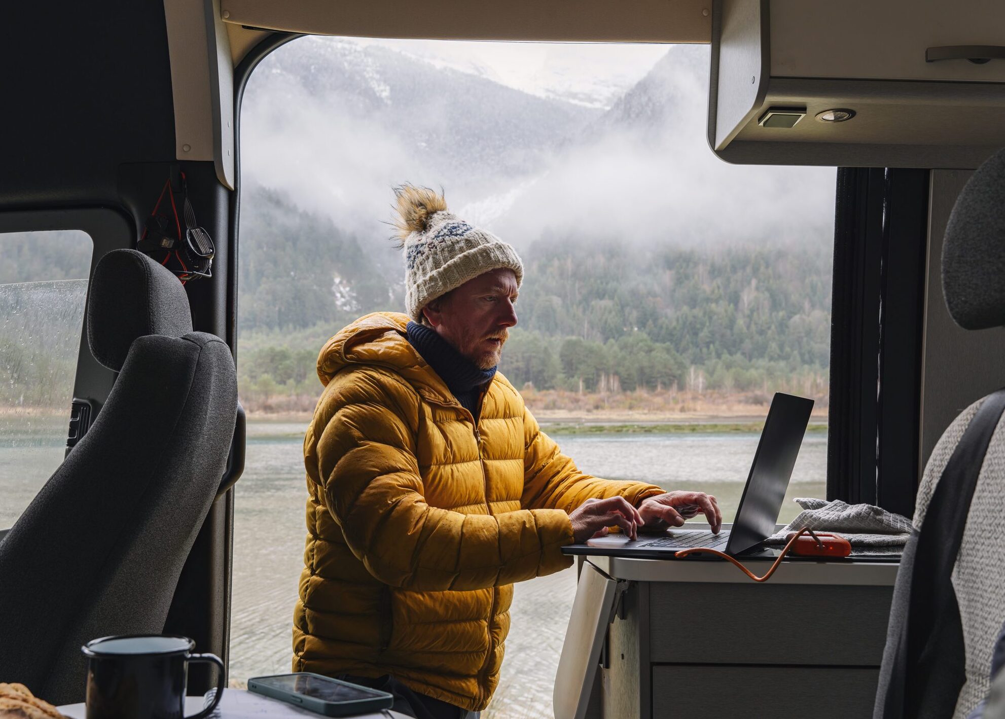 A meteorologist male works remotely from his camper van in the wintry mountains.