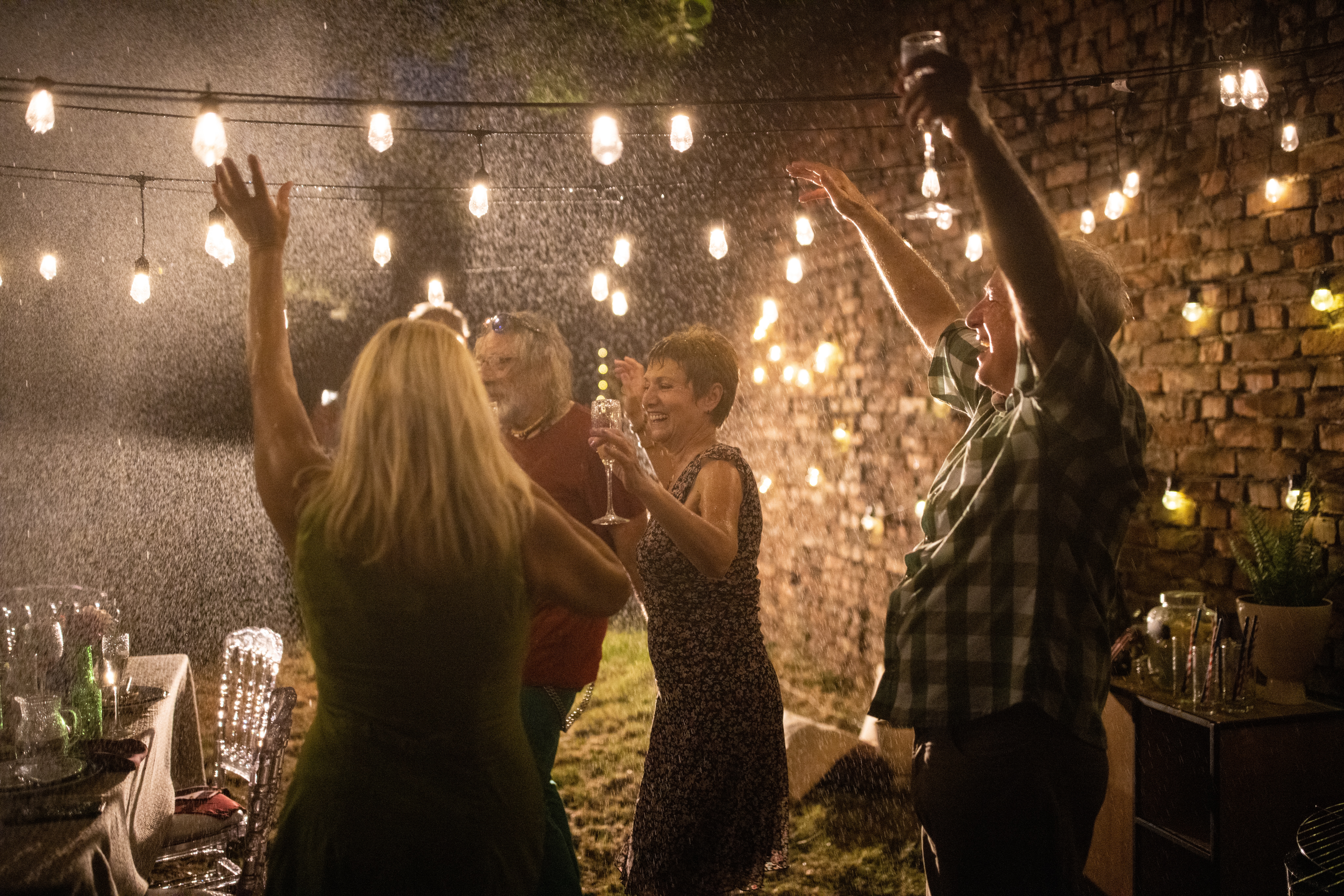 People dancing and enjoying party despite the rain at backyard, at night.