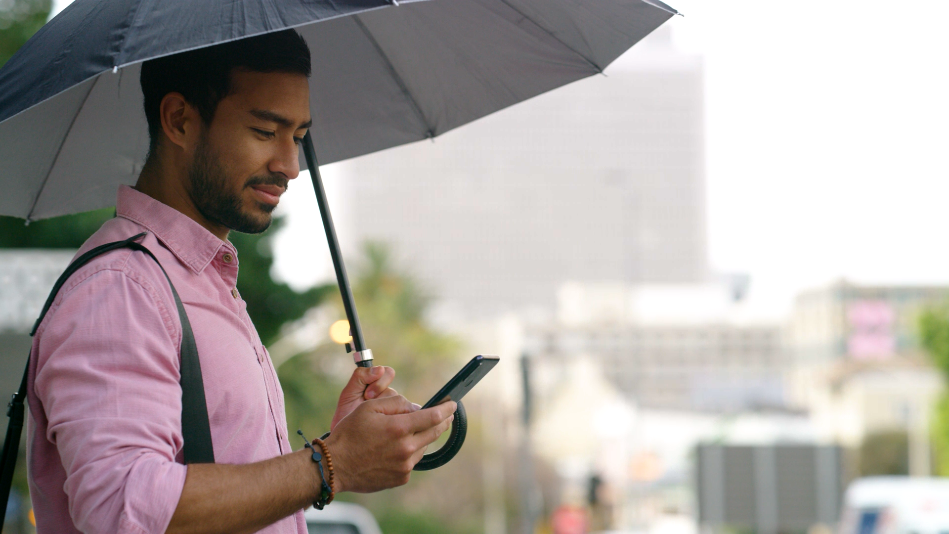man on a city street with an umbrella checking a mobile phone